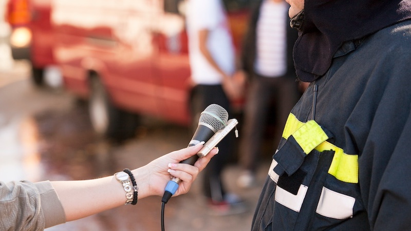 journalist holding a mic to interview someone in a fireman uniform